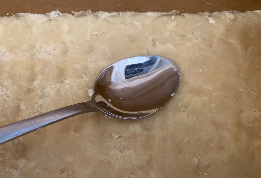 Caramel Shortcake Recipe - Smoothing shortbread into the tin with the back of a spoon