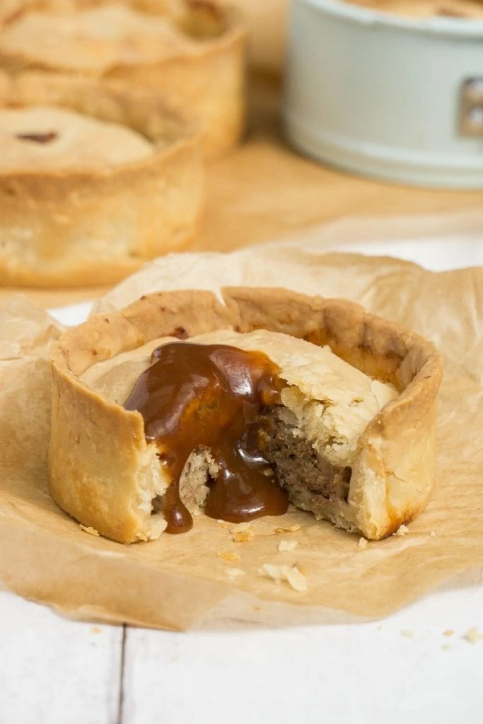 Scotch Pie covered in brown sauce with other scotch pies in the background. 