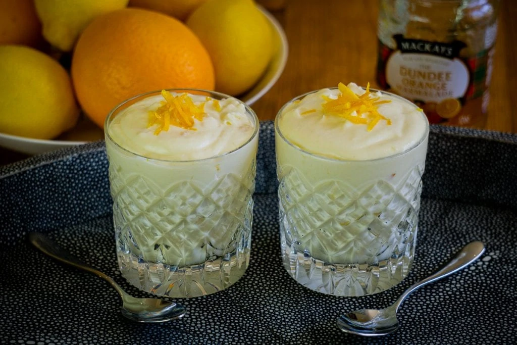 Two glasses of Caledonian Cream on a tray with Dundee Marmalade and oranges