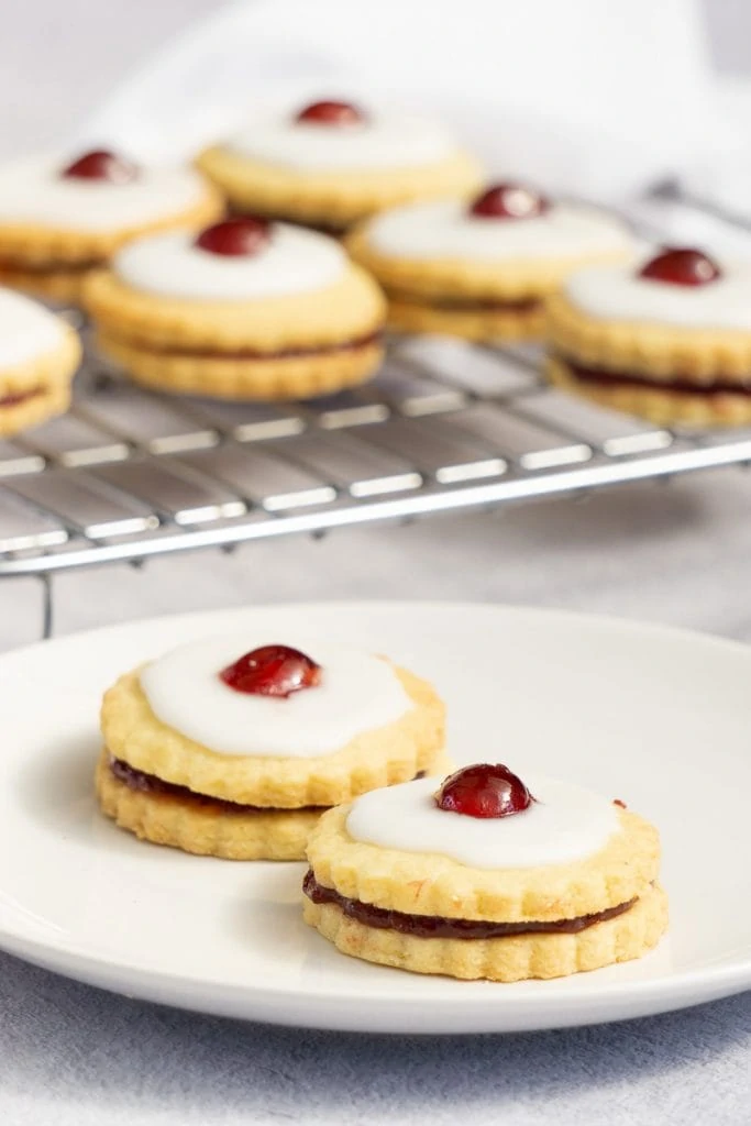 Empire Biscuit Recipe - Double Biscuits with jam, icing and a cherry on a plate and cooling rack