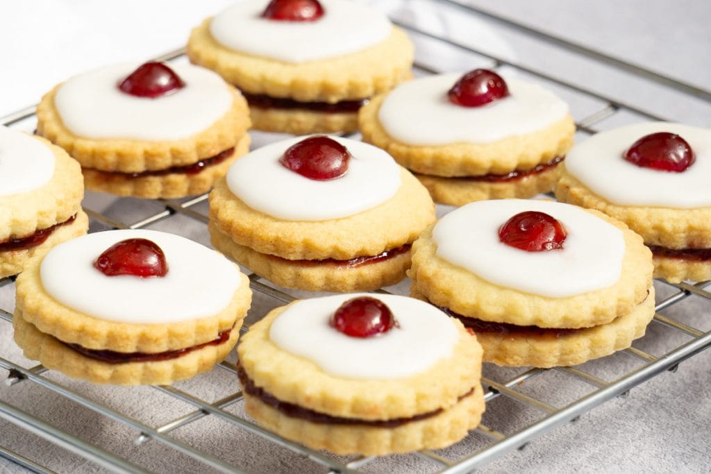 Scottish Empire Biscuits on a rack - Shortbread sandwiched with jam, iced and with a cherry on top