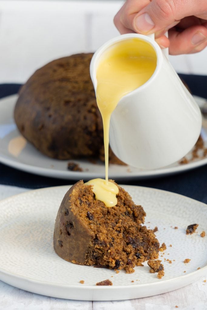 Clootie dumpling and custard being poured over it from a jug