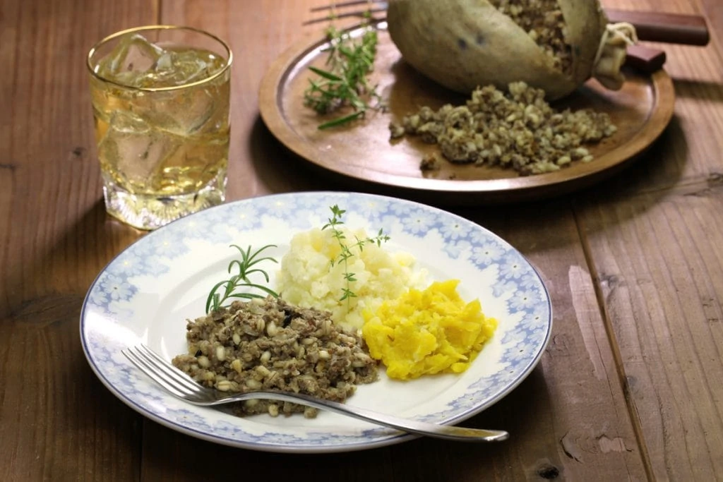 Haggis Neeps and Tatties on a plate with whisky beside for a Burns Supper Menu