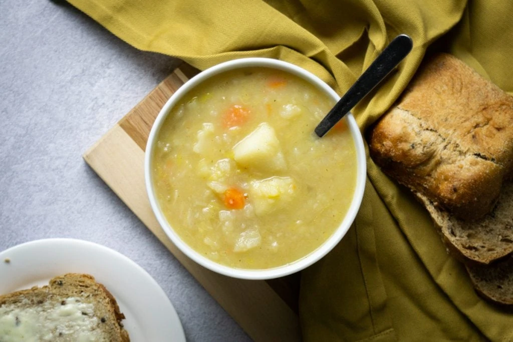 Scottish Potato Soup and Tattie Soup Recipe in a bowl looking from above with bread and potatoes beside