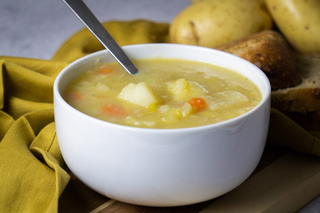 Scottish Potato Soup and Tattie Soup Recipe in a bowl with bread and potatoes beside