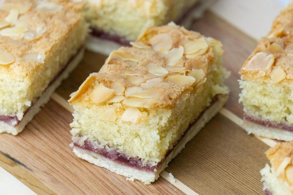 Almond Slice Recipe with slices on a wooden board - Pastry layer, topped with jam and almond sponge