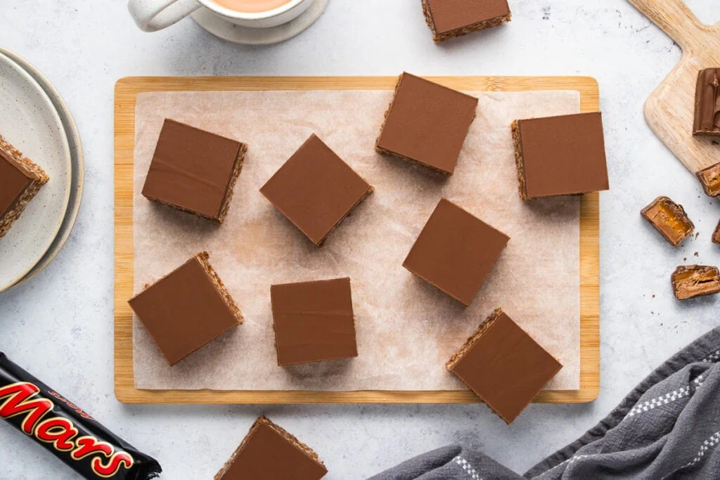 Mars Bar Slice on a chopping board with mars bars around. Also known as mars Bar Squares