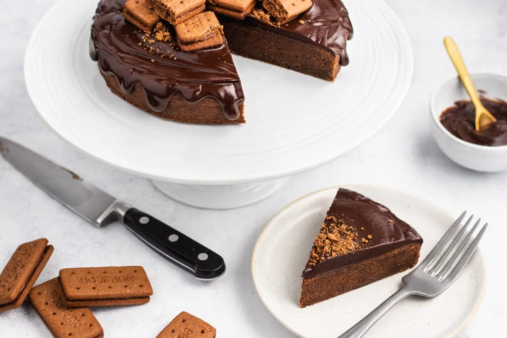 4 Ingredient Bourbon Biscuit Cake Recipe on a cake stand with a slice on a plate, extra biscuits and ganache beside