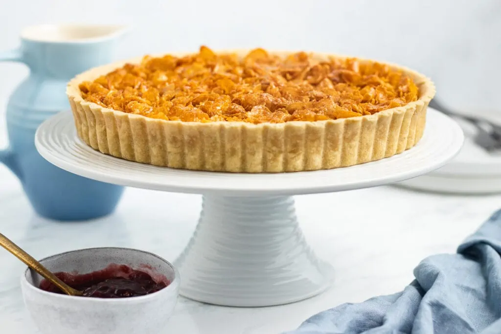 Cornflake Tart Recipe - Tart on a cake stand with bowl of jam and custard next to it. 