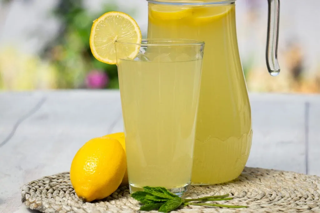 Homemade Lemon Cordial Recipe - a jug and a glass of lemon cordial with lemons and mint on the side