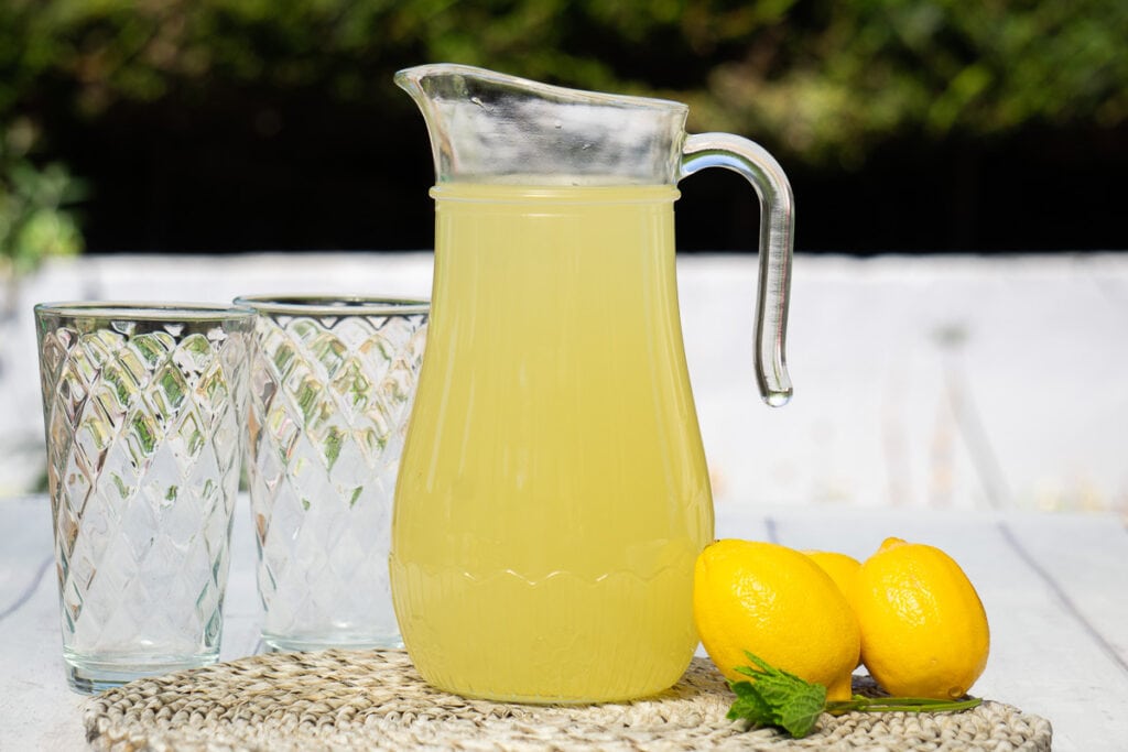 Homemade Lemon Cordial Recipe - two empty glasses and lemon cordial mixed in a jug with lemons on the side
